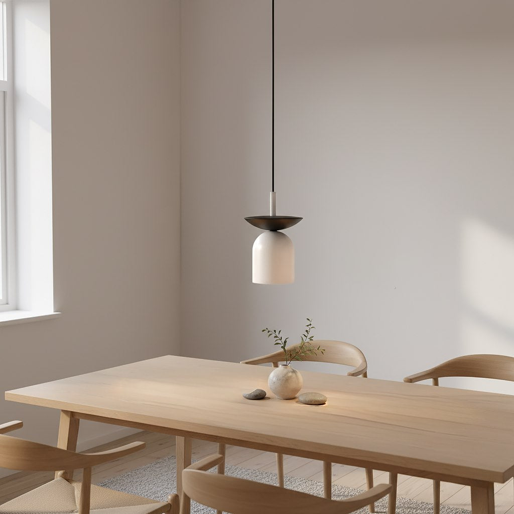 Witte hanglamp met zwart bovenschaaltje en dun zwart snoer boven een houten eettafel met stoelen