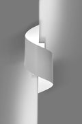 Witte gedraaide wandlamp Spiner aan een grijze muur die zacht licht langs de wand werpt