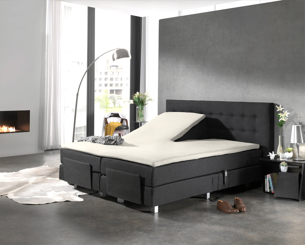 Crèmekleurige splittopper op een antracietkleurige boxspring met één verstelde bedhelft in een moderne slaapkamer