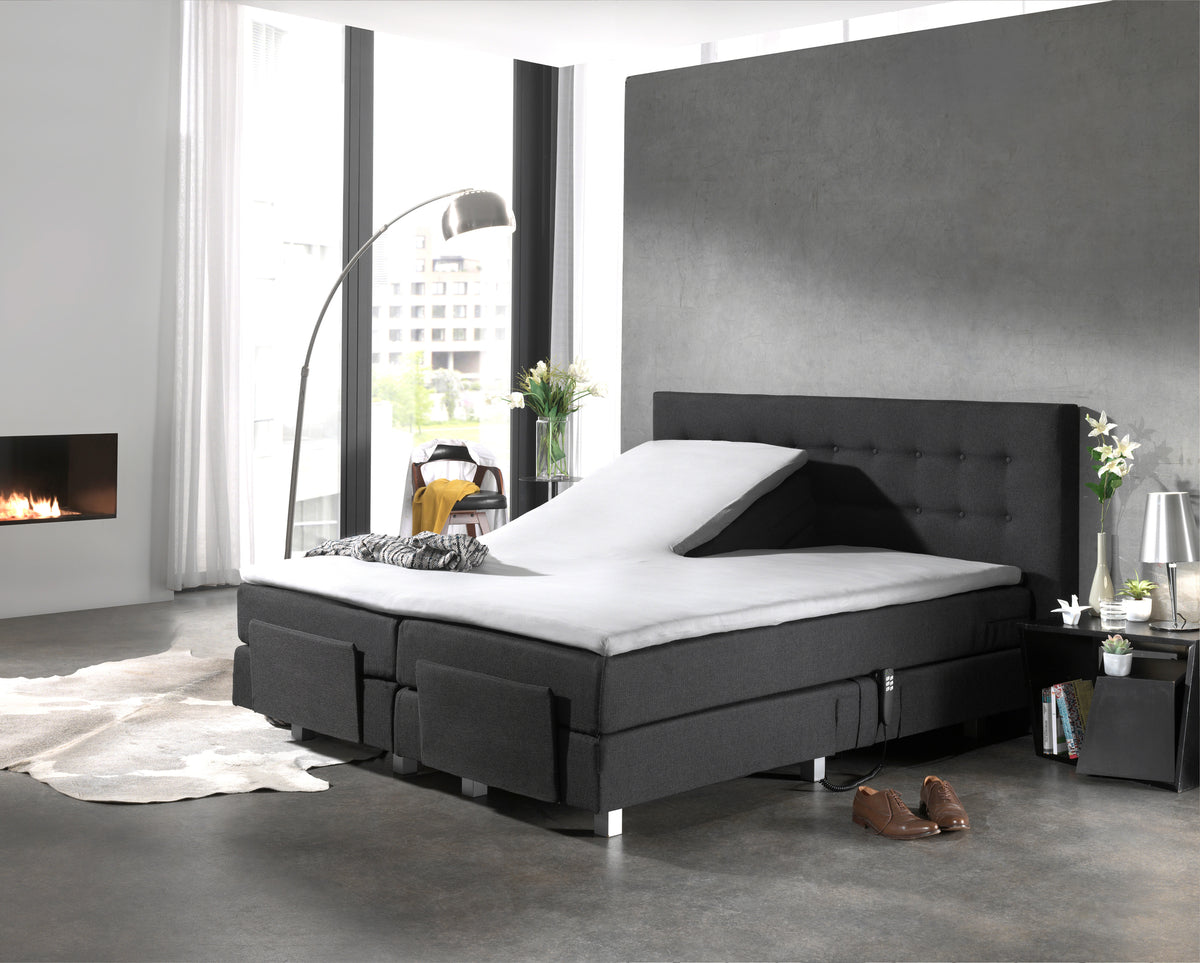 Wit splittopper hoeslaken op een antracietkleurige elektrische boxspring met opgeklapt hoofdeinde in een moderne slaapkamer