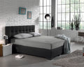 Grijs jersey hoeslaken op een boxspring met donkergrijs hoofdbord in een slaapkamer met witte bakstenen muur