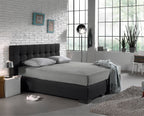 Grijs jersey hoeslaken op een boxspring met donkergrijs hoofdbord in een slaapkamer met witte bakstenen muur