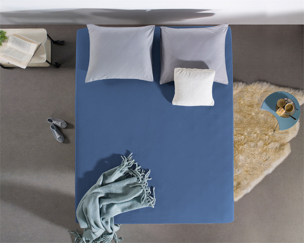 Blauw jersey hoeslaken op een bed met twee lichtgrijze kussens en een wit sierkussen, gezien van boven