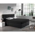 Zwart hoeslaken op een boxspring met donker gecapitonneerd hoofdbord en grijze kussens in een industriële slaapkamer