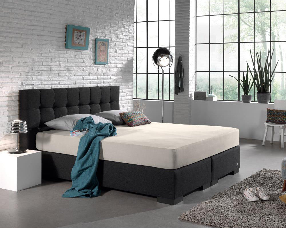 Crème hoeslaken van jersey op een boxspring met donkergrijs hoofdbord in een industriële slaapkamer