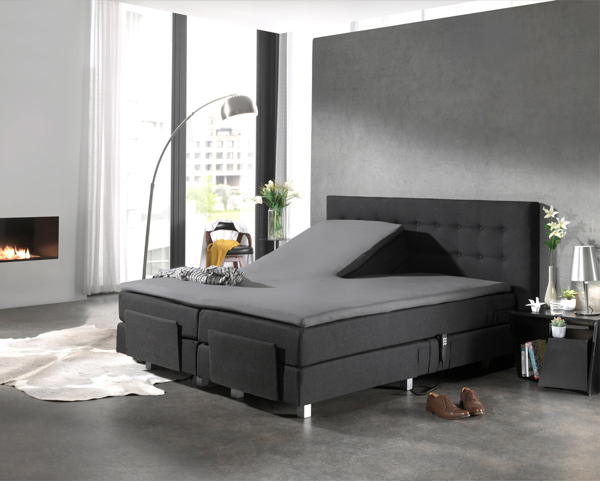 Grijs hoeslaken op een split-topper van een donkergrijze boxspring met hoofdeinde in een moderne slaapkamer