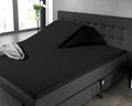 Zwart hoeslaken op een splittopper van een donkergrijs boxspringbed, met één opgetilde topperhelft