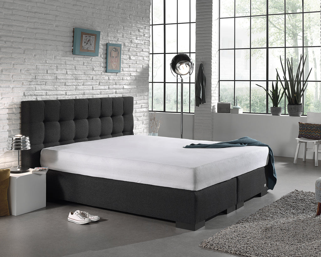 Wit molton hoeslaken om een matras op een antracietkleurig boxspringbed met gecapitonneerd hoofdbord