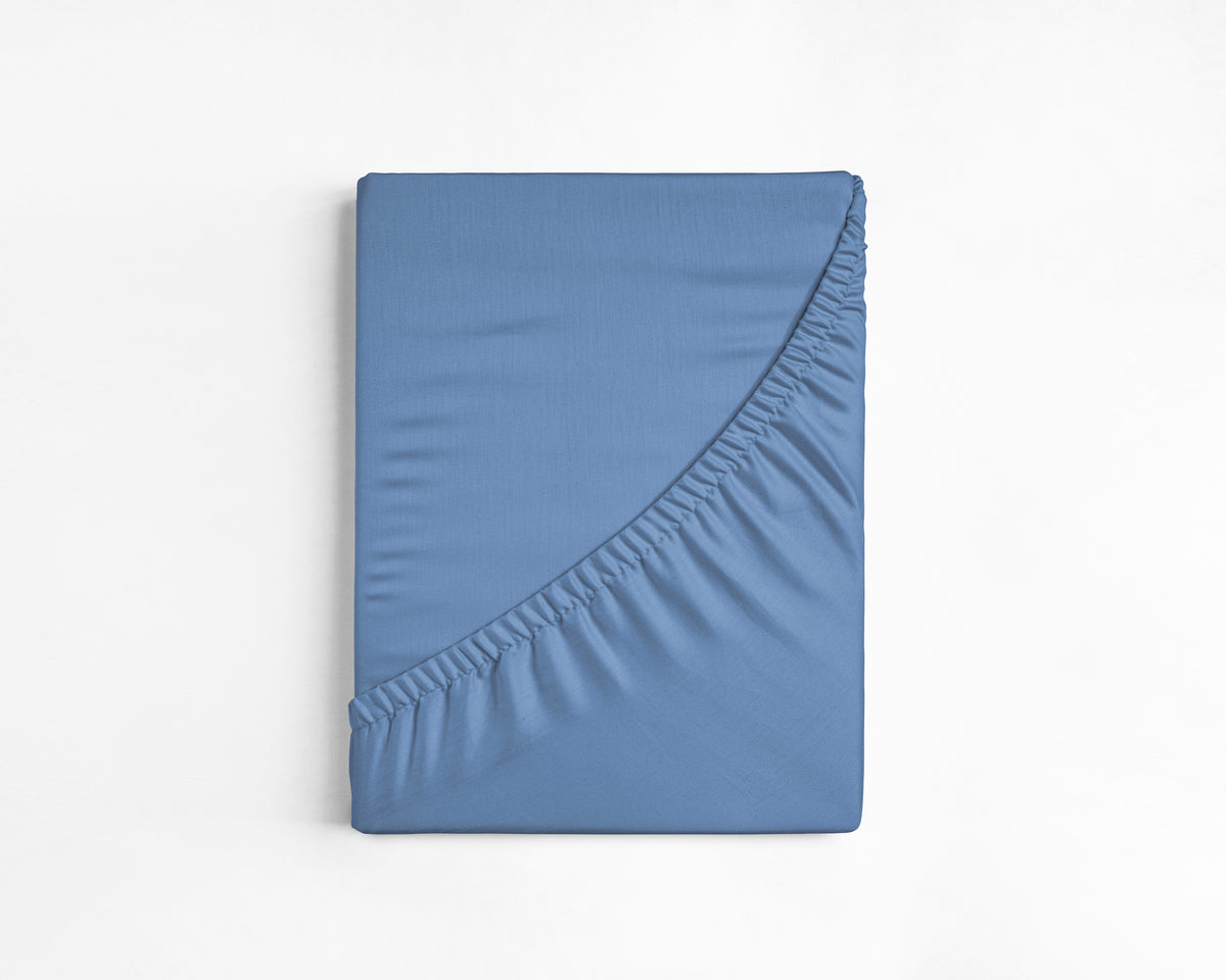 Opgevouwen blauw hoeslaken van katoen met zichtbare elastische rand tegen een witte achtergrond