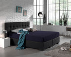 Marineblauw hoeslaken op een boxspring met donker gecapitonneerd hoofdbord in een lichte slaapkamer