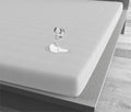 Wit waterdicht hoeslaken op een matras waarop een omgevallen glas water een plas vormt zonder in te trekken