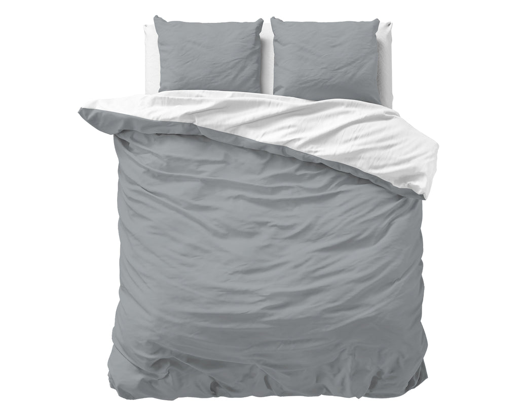 Omkeerbaar dekbedovertrek grijs met witte binnenkant en twee grijze kussens op een bed
