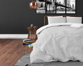 Bed opgemaakt met lichtgrijs dekbedovertrek en kussens voor een donkere muur met koperkleurig bedframe