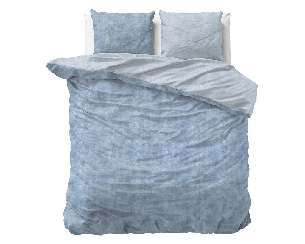 Opgemaakt bed met blauw gewassen flanel dekbedovertrek, omgeslagen lichtgrijze binnenkant en twee bijpassende kussens