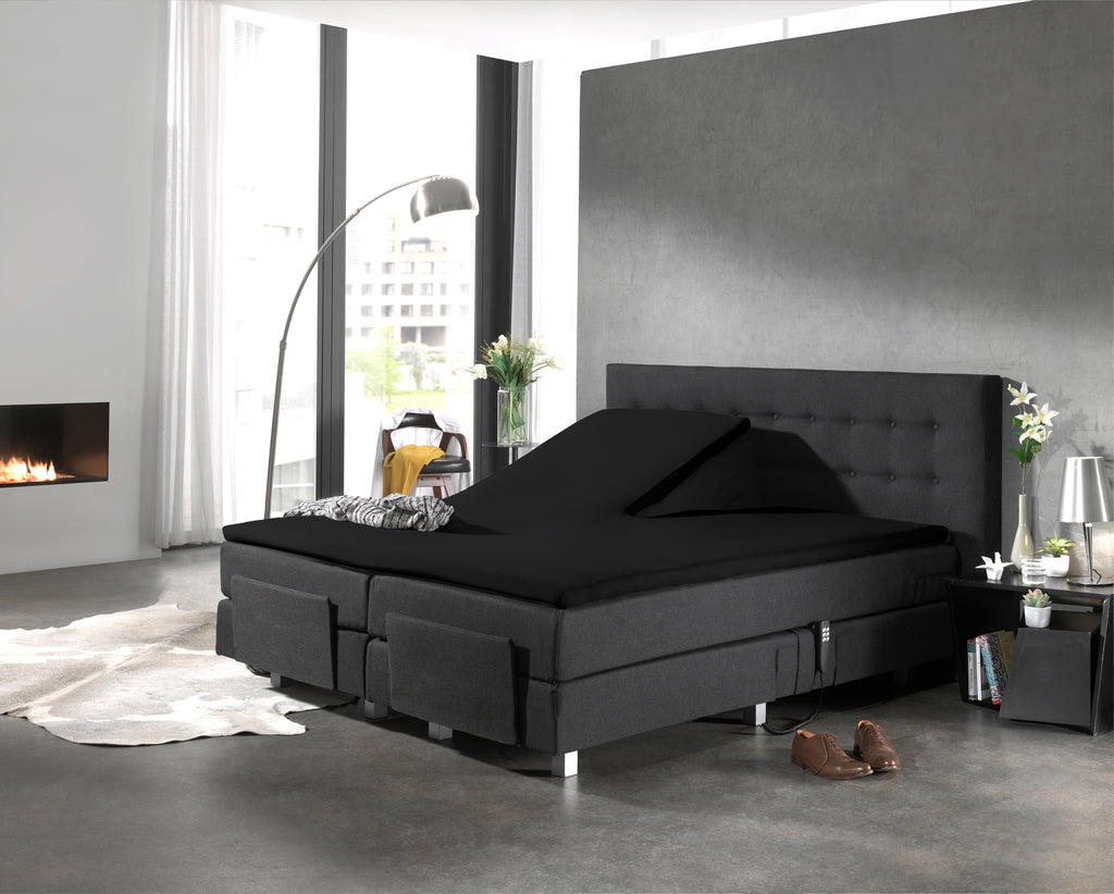 Zwart splittopper hoeslaken op een antraciet boxspring met knoopjes in het hoofdbord in een moderne slaapkamer