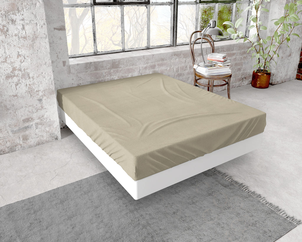 Taupe hoeslaken van flanel over een matras op een wit bedframe in een loft met bakstenen muur en groot raam