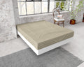 Taupe hoeslaken van flanel over een matras op een wit bedframe in een loft met bakstenen muur en groot raam