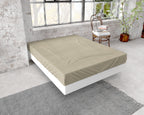 Taupe hoeslaken van flanel over een matras op een wit bedframe in een loft met bakstenen muur en groot raam