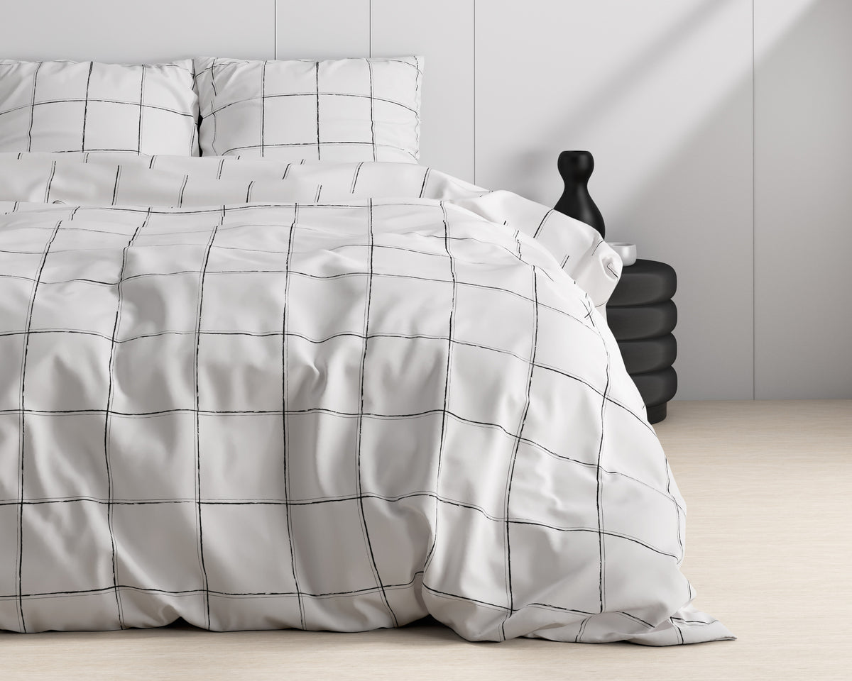 Wit dekbedovertrek met zwarte ruitprint op een bed, naast een zwart bijzettafeltje en zwarte vaas