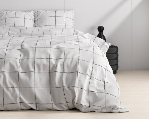 Wit dekbedovertrek met zwart ruitpatroon op een opgemaakt bed, met zwarte vaas en zwart bijzettafeltje ernaast