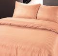 Pastel oranje dekbedovertrek met geëmbosseerde hotelstrepen en twee bijpassende kussens op een bed