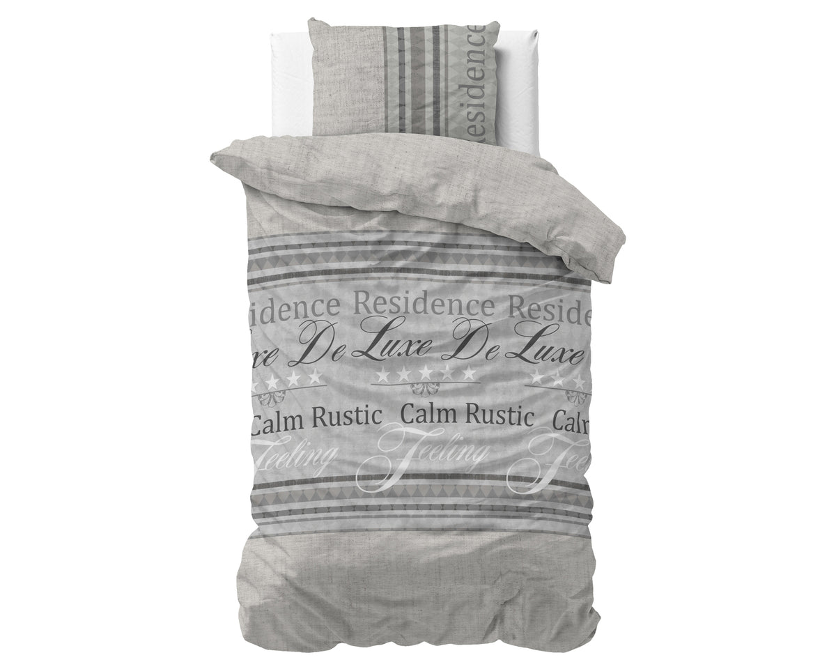 Grijs dekbedovertrek met tekstprint Residence De Luxe en Calm Rustic Feeling, met bijpassende kussensloop op een bed