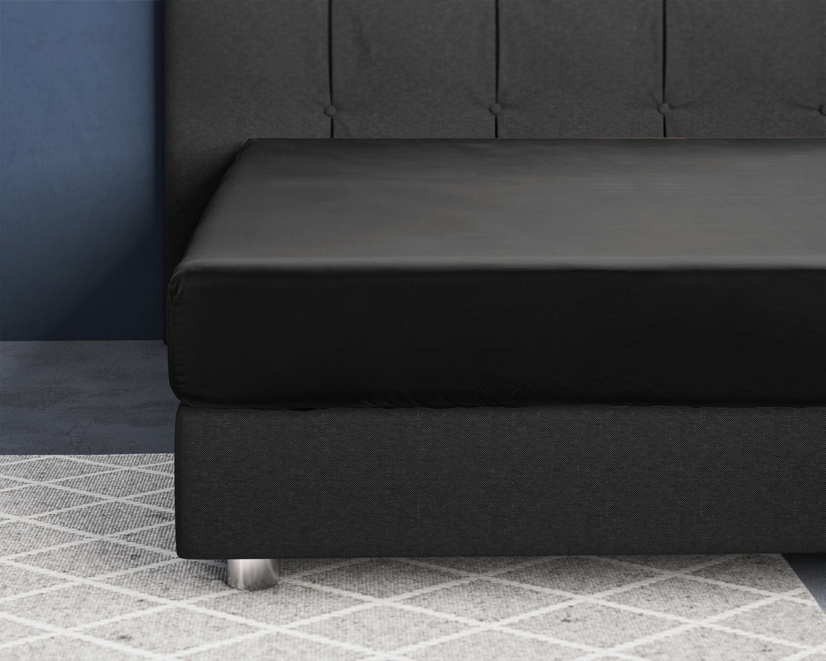 Zwart satijnen hoeslaken om een matras op een donkergrijs bed met gecapitonneerd hoofdbord