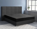 Zwart satijnen hoeslaken om een matras op een boxspring met grijs gecapitonneerd hoofdbord in een slaapkamer