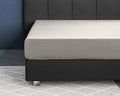 Crèmekleurig satijnen hoeslaken om een matras op een donkergrijs boxspringbed met gecapitonneerd hoofdbord