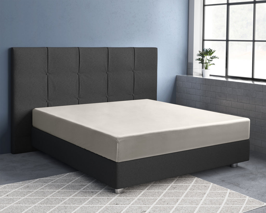 Crèmekleurig satijnen hoeslaken op een matras met donkergrijs gestoffeerd hoofdbord en donkere onderbouw