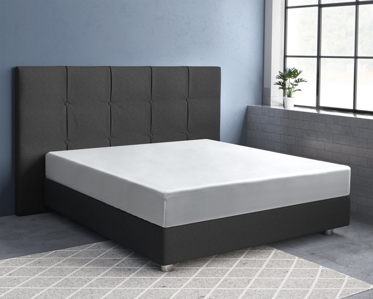 Wit hoeslaken om een matras op een donkergrijs bed met gecapitonneerd hoofdbord in een slaapkamer met blauwe muur