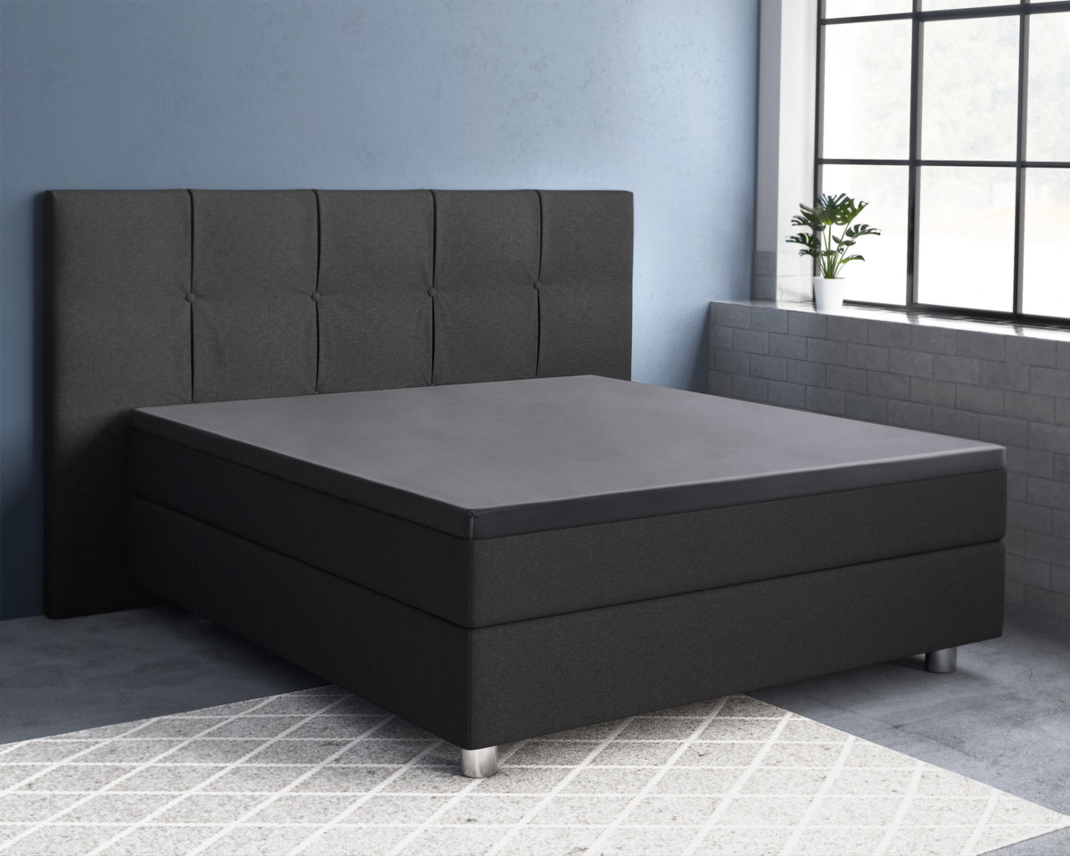 Antracietkleurig boxspringbed met gestoffeerd hoofdbord en donker topperlaken op het matras in een slaapkamer