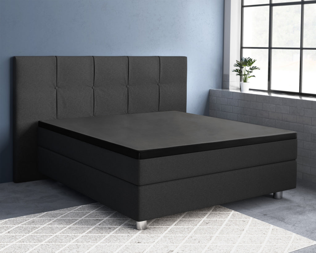 Zwart topperhoeslaken op een antracietkleurig boxspringbed met gecapitonneerd hoofdbord in een slaapkamer