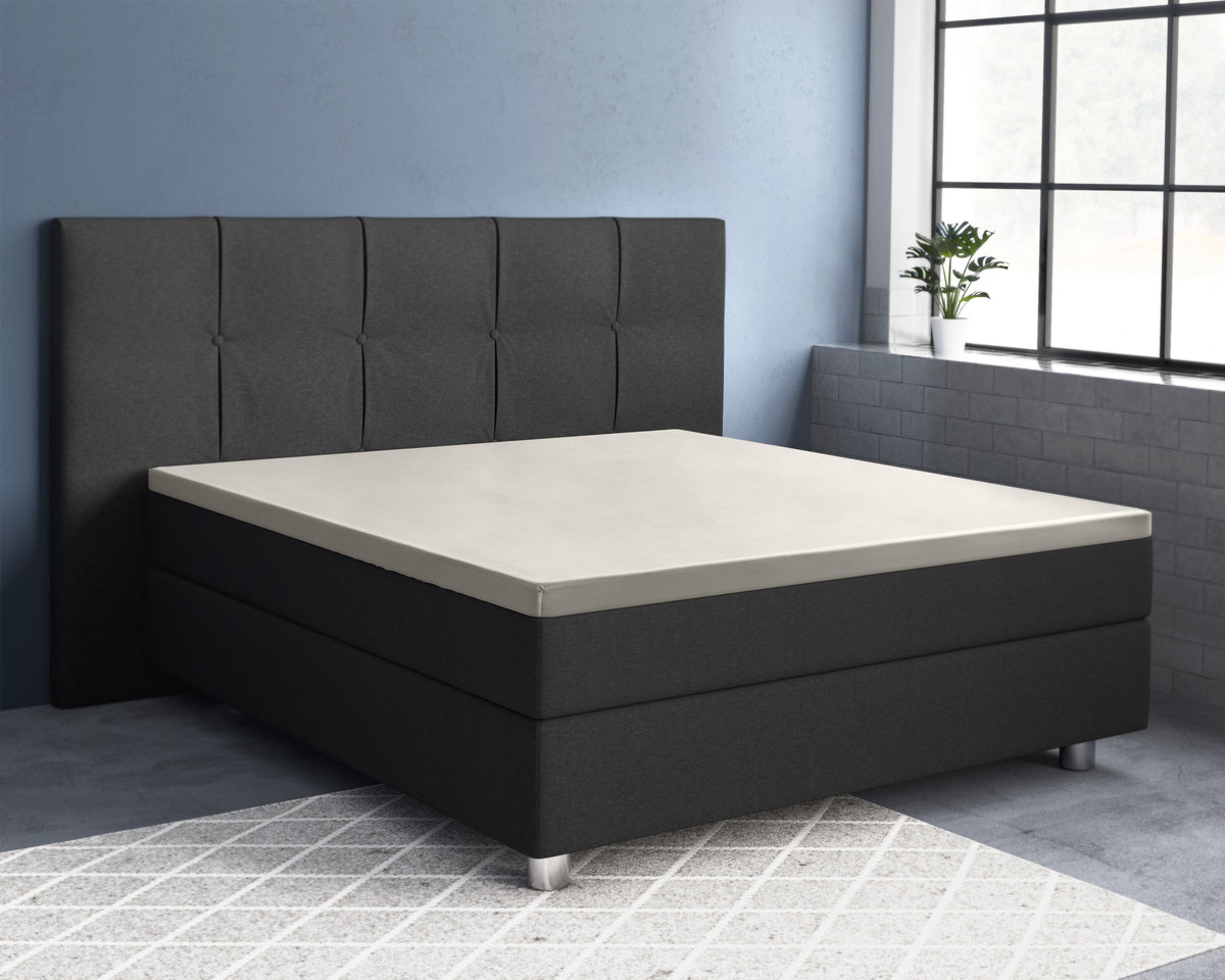Crèmekleurig topper hoeslaken op een donkergrijs boxspringbed met gestoffeerd hoofdbord in een slaapkamer met blauwe muur