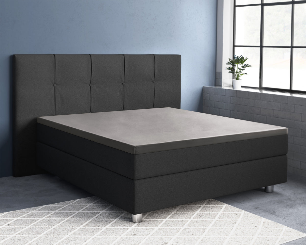 Grijs topper hoeslaken op een zwarte boxspring met gestoffeerd hoofdbord in een kamer met blauwe muur