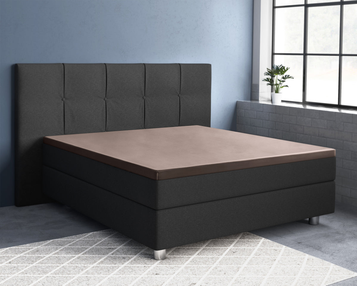 Taupe satijnen topper hoeslaken op een donkergrijs boxspringbed met hoofdbord in een slaapkamer