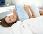 Vrouw ligt op bed met een wit hoofdkussen met blauw ruitpatroon en blauwe bies in haar armen