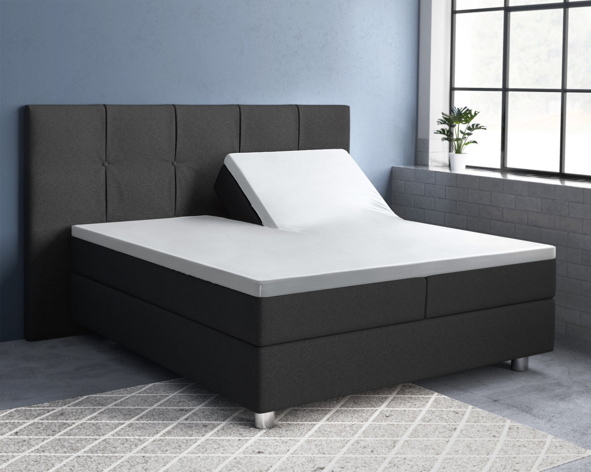 Wit satijnen splittopper hoeslaken op een donkergrijs bed, met de ene helft van de topper omhoog verstelbaar
