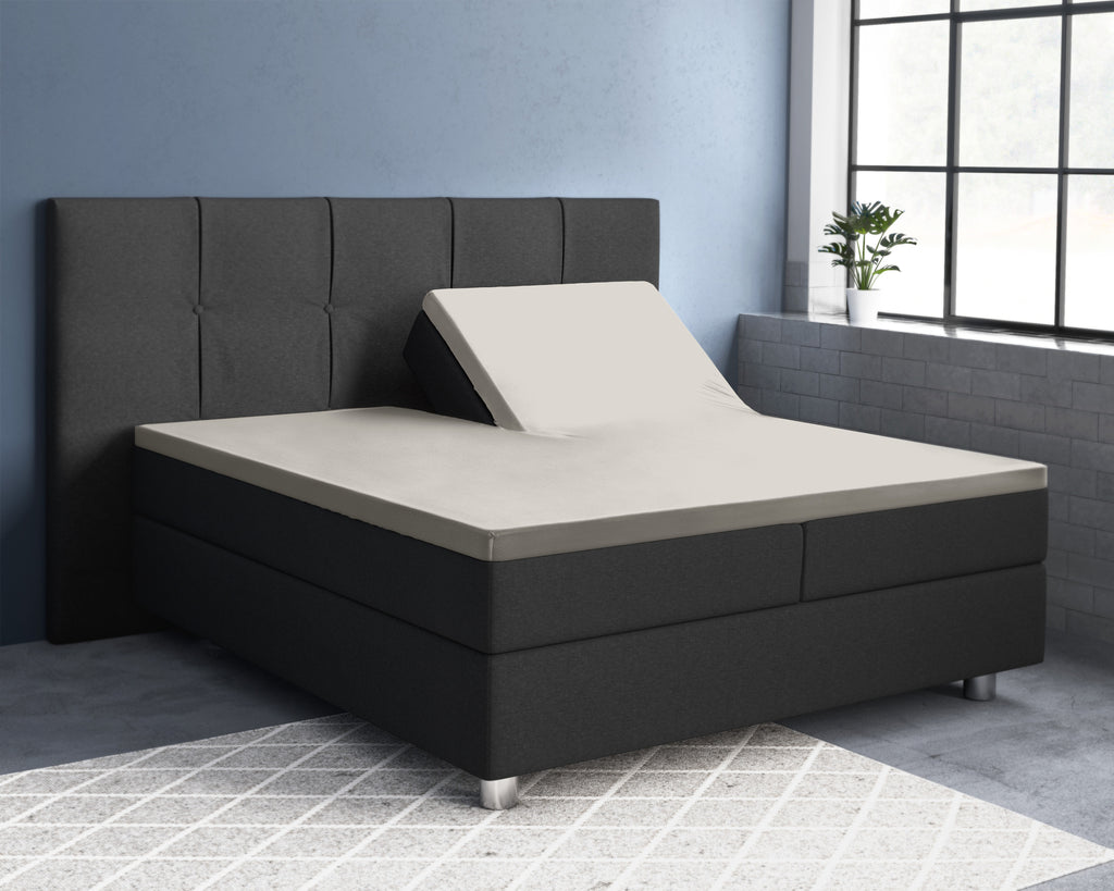 Crèmekleurig splittopper hoeslaken op een verstelbaar boxspringbed met donkergrijs hoofdbord, één helft omhoog