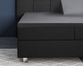 Antraciet splittopper hoeslaken van satijn over een donkergrijze boxspring op een grijs geruit vloerkleed