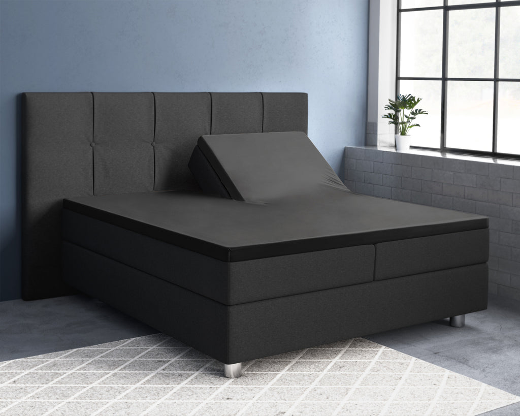 Zwart splittopper hoeslaken op een donkergrijze boxspring met verstelbaar hoofdeinde in een slaapkamer met blauwe muur