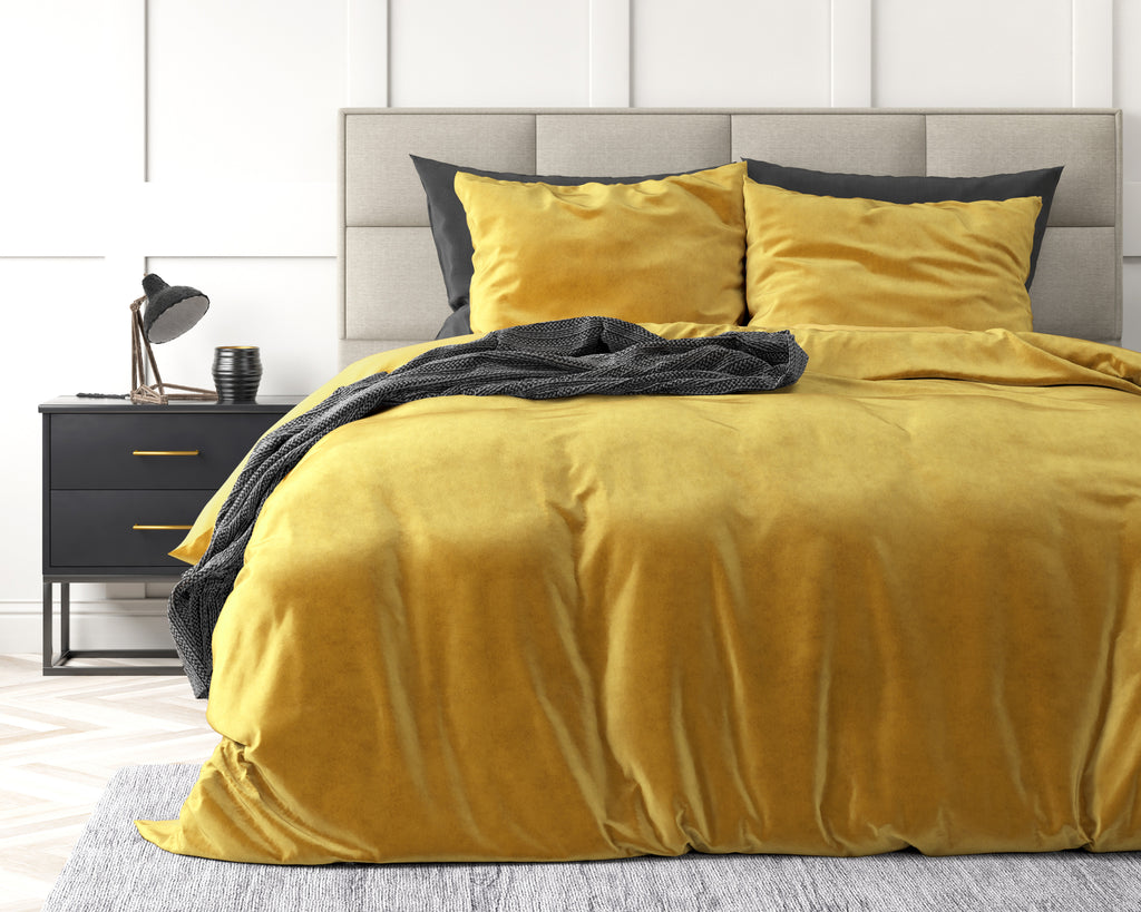 Goudkleurig velvet dekbedovertrek met kussenslopen op een bed met grijs hoofdbord en antracietkleurige plaid