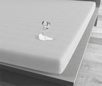 Wit waterdicht hoeslaken op een matras met een omgevallen glas en gemorst water dat op het laken blijft liggen