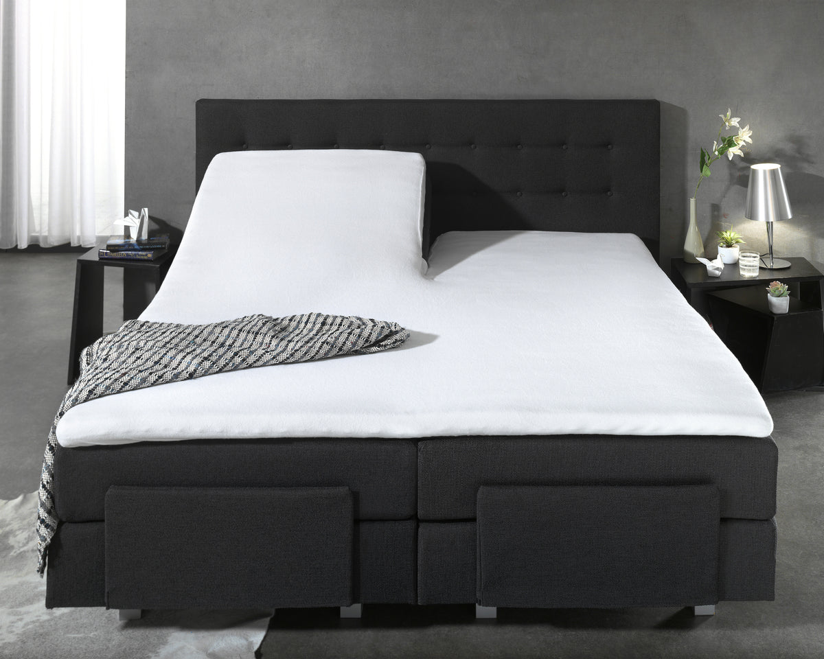 Wit waterdicht split hoeslaken op een verstelbaar donkergrijs boxspringbed met gestoffeerd hoofdbord