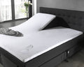 Wit waterdicht splittopper hoeslaken op verstelbaar bed met omgevallen glas en gemorst water op het laken