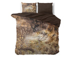 Dekbedovertrek met taupe print en goudkleurige accenten, omgeslagen met effen bruine binnenzijde en twee kussens op bed