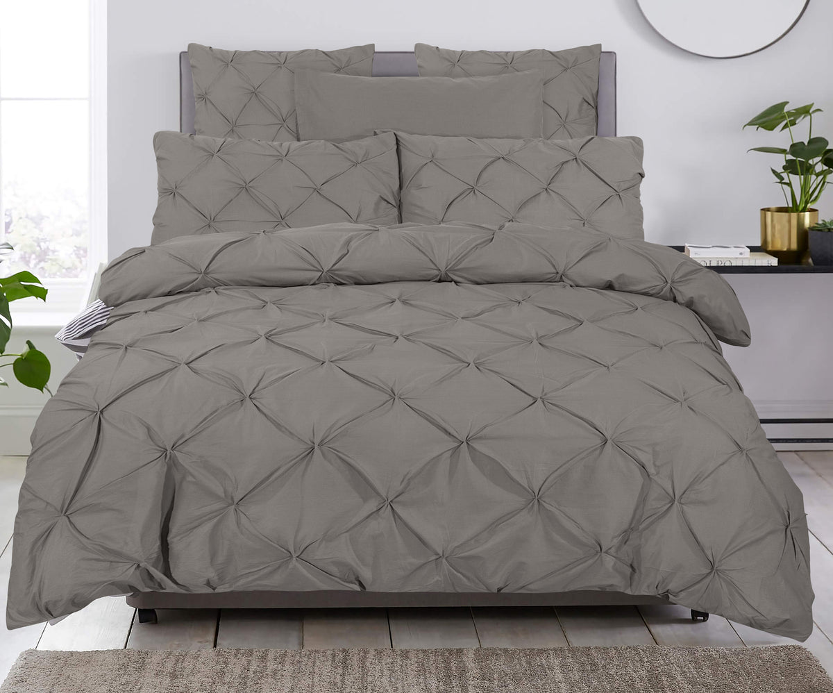 Bed opgemaakt met taupe pintuck dekbedovertrek en bijpassende kussenslopen in een lichte slaapkamer
