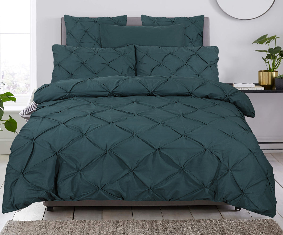 Bed met donkergroen pintuck dekbedovertrek en bijpassende kussenslopen in een lichte slaapkamer