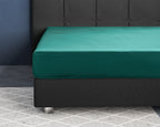 Donkergroen hoeslaken van katoensatijn over een matras op een donkergrijs bed met gecapitonneerd hoofdbord
