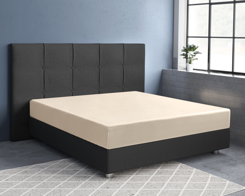 Zandkleurig satijnen hoeslaken op een bed met donker gestoffeerd hoofdbord en boxspring voor een blauwe muur
